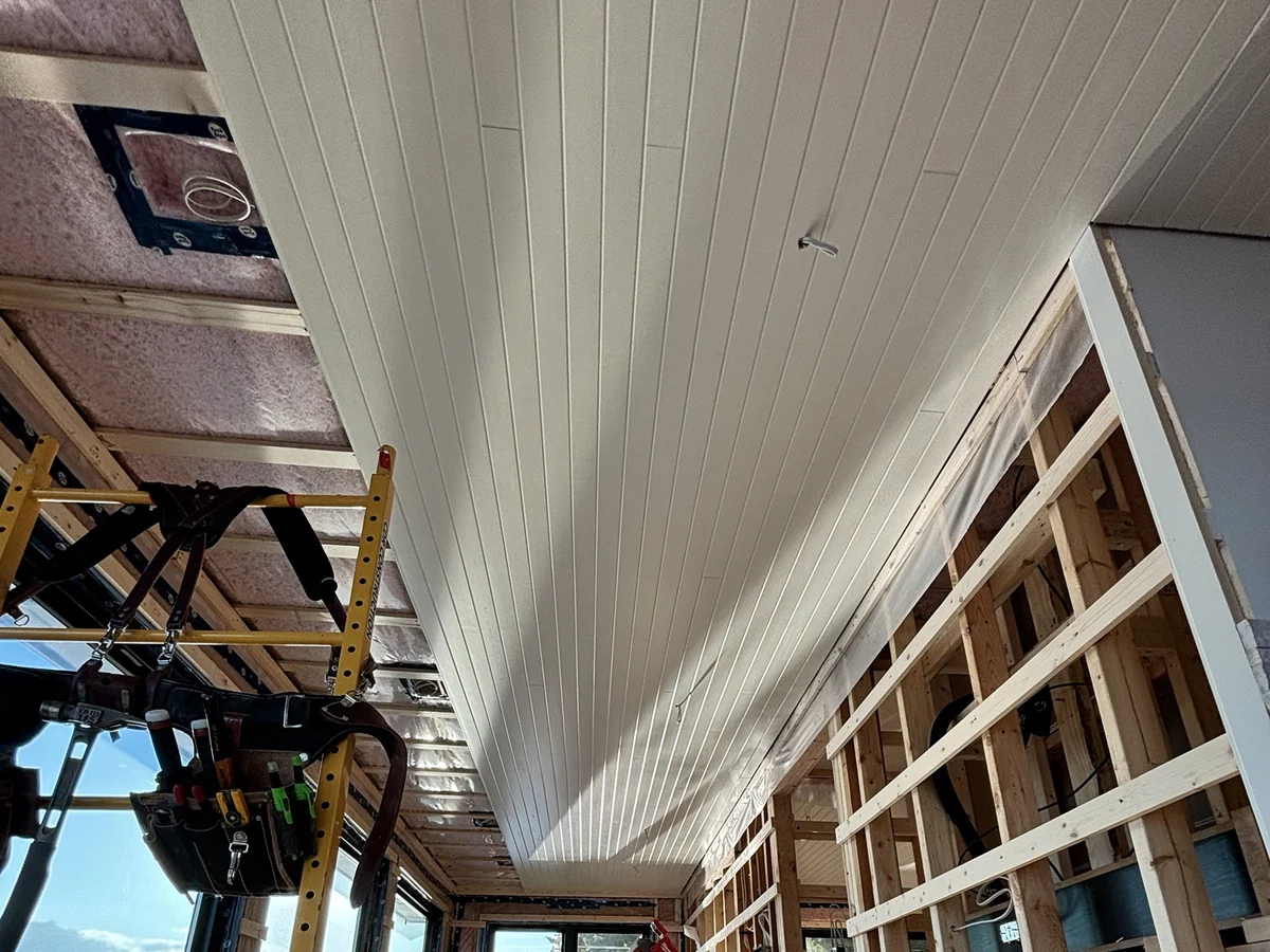 White V-groove ceiling boards being installed down a long room